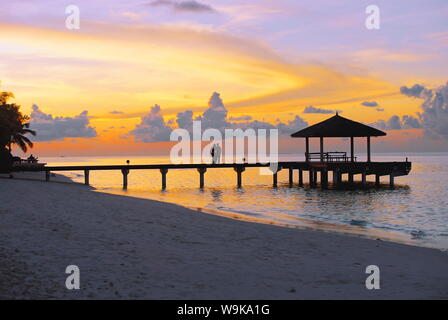 Paar am Steg mit Blick auf den Sonnenuntergang, Malediven, Indischer Ozean, Asien Stockfoto