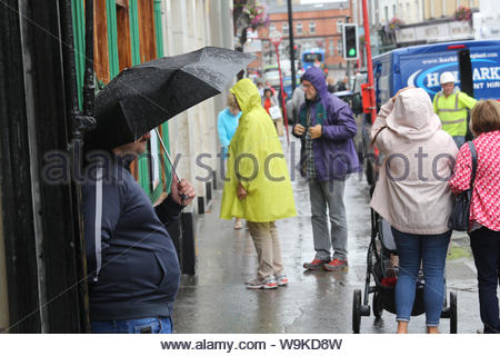 Ein Mann Unterstände unter einem Sonnenschirm während einer schweren Dusche im Zentrum von Sligo, Irland, heute Nachmittag. Die Prognose für die weitere wechselhafter Witterung in den nächsten Tagen. Stockfoto