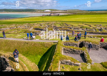 Touristen, die in der Nordischen Siedlung ausgegraben Jarlshof in der Nähe von Sumburgh Head im Süden von Mainland, Shetland. West Voe von sumburgh im Hintergrund. Stockfoto