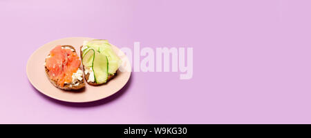Essen und richtige Ernährung Konzept. Leckere frische Sandwich mit roten Fischen, Feta Käse Gurken und Pesto auf einem rosa Keramikplatte auf einem violetten Hintergrund Stockfoto