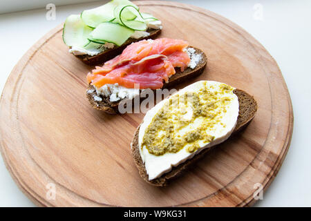 Essen und richtige Ernährung Konzept. Leckere frische Sandwich mit roten Fischen, Feta Käse Gurken und Pesto auf einem rosa Keramikplatte auf einem Holzbrett Stockfoto