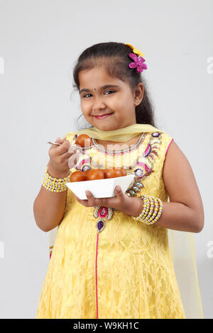 Mädchen essen gulab jamun und lächelnd Stockfoto