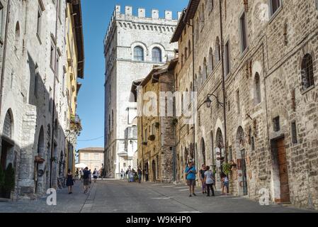 Gubbio, Italien - 11 August, 2019: Touristen, die sich in der zentralen Straße der umbrischen Stadt, mit dem Palazzo dei Consoli im Hintergrund Stockfoto