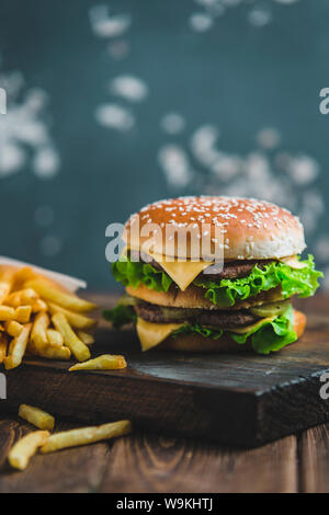 Burger mit Kartoffeln und dunkles Bier auf einem Holzbrett auf ein blau-grauer Hintergrund Stockfoto