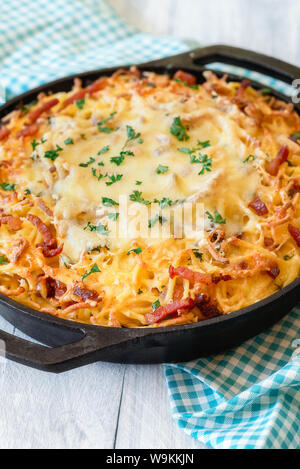 Leckere deutsche Käse Spätzle in eine rustikale Gusseisen Fach auf eine Bayerische Küche Handtuch. Nahaufnahme der Schwäbische Eiernudeln mit geschmolzenem Käse. Hausgemachte Teller Stockfoto