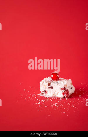 Ein Stück der Australischen Weihnachten dessert Hausgemachte mit Kokos und getrocknete Früchte, auf einem roten Hintergrund. Close-up mit traditionellen White Christmas Cake. Stockfoto