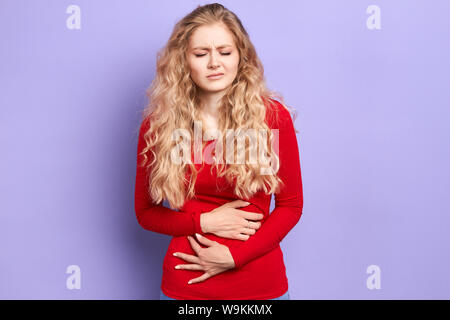 Schöne arme Frau mit langen Messe gewelltes Haar hat Probleme mit dem Magen, schmerzhafte Menstruation. Fehlgeburt Konzept. Isolierte hellblauen Hintergrund Stockfoto