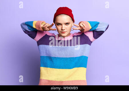 Attraktive Coole Mädchen zeigen v-sign, Hörner, von den Fingern. schließen Foto. Isolierte blauen Hintergrund, Studio erschossen. Körpersprache Stockfoto