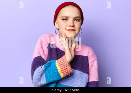 Junge cool womanin gestrickte Pullover und Hut sagen einen geheimen heißen Bremsen Nachrichten und Suchen an der Kamera an. Schließen Sie herauf Foto. Isolierte blauen Hintergrund studio Stockfoto