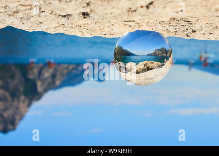 Gardasee (Lago di Garda oder Lago Benaco) gesehen durch eine Glaskristall auf dem Felsen platziert. Selektiver Fokus Stockfoto