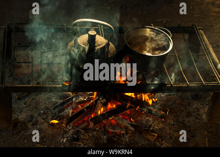 Ein Topf und ein Wasserkocher stehen über einem Feuer auf einem tragbaren Ofen aus Metall Stangen in einem Nomad Wohnung Stockfoto