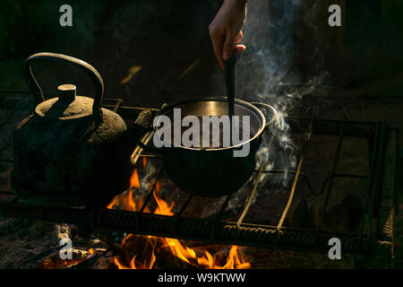 Topf und Wasserkocher stand über einem Feuer auf einem tragbaren Ofen aus Metall Stangen in einem Nomad Wohnung Stockfoto