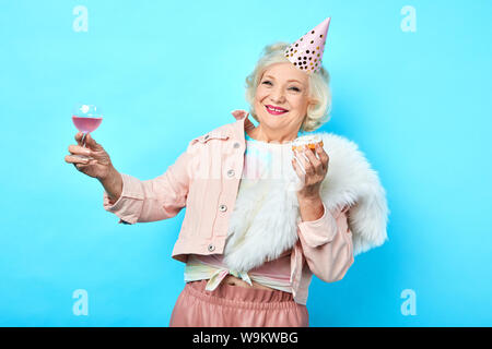 Happy positive Lustig ältere Frau mit Spaß in die Partei. Isolierte blauen Hintergrund. Studio erschossen. Lifestyle. Feier, freie Zeit Stockfoto