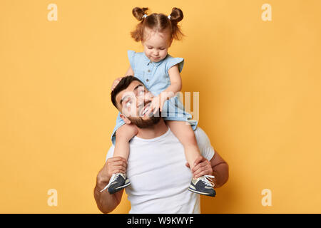 Kleines Mädchen ihrem Vater die Zähne berühren beim Sitzen auf hids Hals. schließen Foto. Isolierte gelben Hintergrund Stockfoto