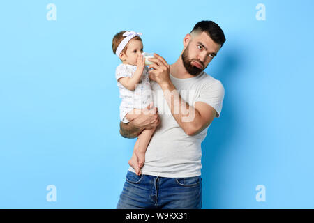 Erschöpft, müde Vater, der sein Baby mit milchflasche. schließen Foto. Isolierte blauen Hintergrund. Studio erschossen. armer Vater ist satt loking afte Stockfoto