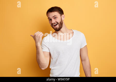 Lustig emotional positiver Mann mit Daumen beiseite angezeigt, isolierte gelben Hintergrund. Studio erschossen. nach oben Foto schliessen. Platz für Text, Werbung. Kopieren Sie spa Stockfoto