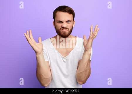 Junge nervöse kaukasischen Mann mit aggressiver Ausdruck und die Arme angehoben in die Kamera schaut. Frustration Konzept. negative Emotion. isolierte Blau ba Stockfoto