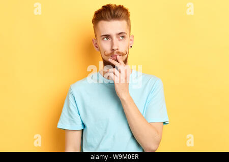 Junger stattlicher Mann mit dem Finger auf seine Lippen, Mund, weg schauen, Denken vor gelbem Hintergrund. nach oben Porträt schließen. Isolierte gelben Hintergrund Stockfoto