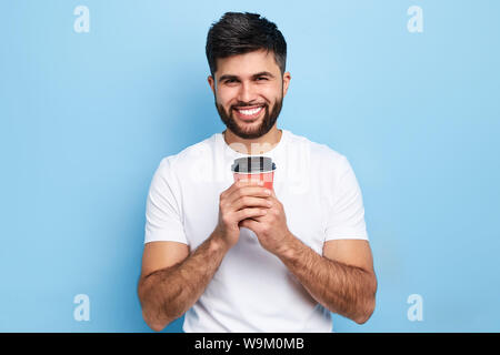 Schöne positive lächelnde Mann mit Tasse Kaffee in der Hand in die Kamera schaut. Auf blauem Hintergrund isoliert. lustige Kerl ist Kaffeepause. positive emo Stockfoto