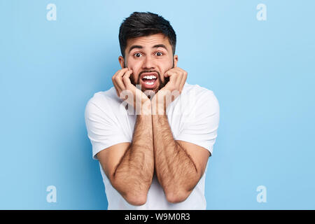 Emotionaler Mensch kann nicht glauben, dass in den Nachrichten, Klatsch, Mann mit Palmen unter sein Kinn auf seine Freundin mit Interesse, bis Portrait schließen, isoliert Blau ba Stockfoto