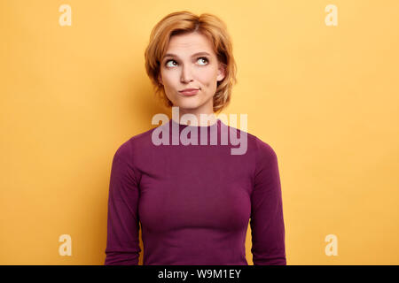 Nachdenklich blonde Mädchen äußern Zweifel und fragen sich, abgesehen suchen, isolierte gelben Hintergrund, Studio gedreht. Stockfoto