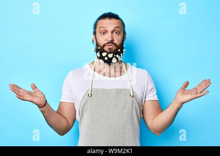 Junger bärtiger Mann mit grauen Schürze und Achselzucken über blau Hintergrund isoliert verwirrt. Gestik, Körpersprache. Stockfoto
