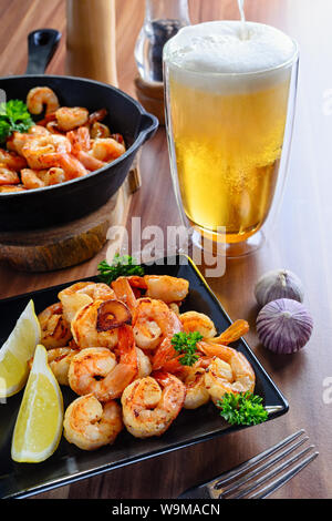 Ein Glas goldenen Bier mit leckeren gegrillten Garnelen auf Holztisch, Nahaufnahme Stockfoto