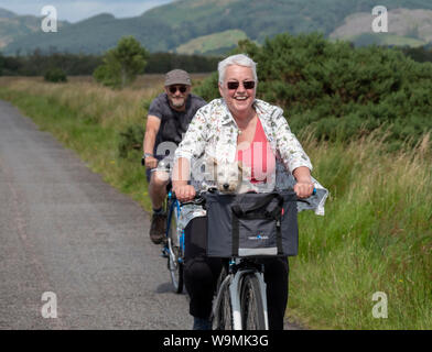 Portrait Of Happy Radfahrer mit einem kleinen Hund in ihrem Fahrrad Korb in der Nähe von Crinan, Argyll. Stockfoto