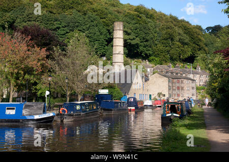 Narrowboats auf dem Rochdale Canal an Hebden Bridge mit alten Schornstein der Crossley Mühle in der Ferne, Obere Calder Valley, West Yorkshire Stockfoto