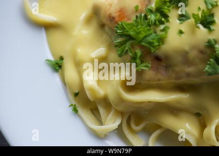 Das Essen : In der Pfanne gebratener Lachs auf einem Bett von Tagliatelle mit Sauce Hollandaise und gehackte Petersilie auf einem weißen Teller serviert Stockfoto