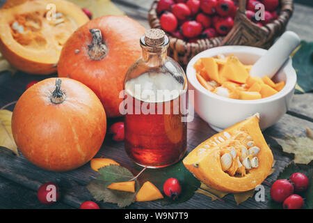 Kürbiskerne öl Flasche, Kürbisse, Mörtel und Korb von Weißdorn-Beeren auf Holztisch mit Blätter im Herbst. Stockfoto