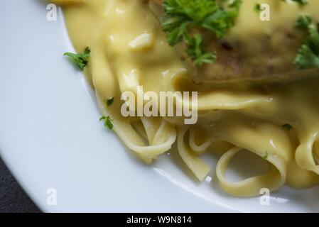 Das Essen : In der Pfanne gebratener Lachs auf einem Bett von Tagliatelle mit Sauce Hollandaise und gehackte Petersilie auf einem weißen Teller serviert Stockfoto