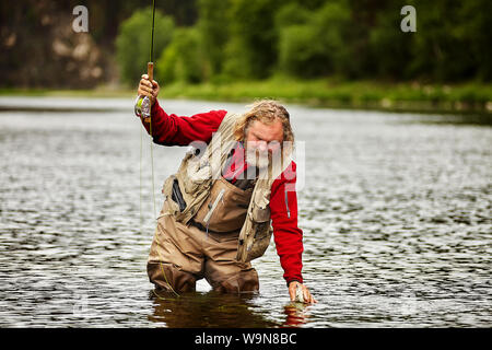 Reifen bärtigen Fischer in Wasser stehend mit Stab in seiner Hand und versuchte die Fische zu fangen. Stockfoto