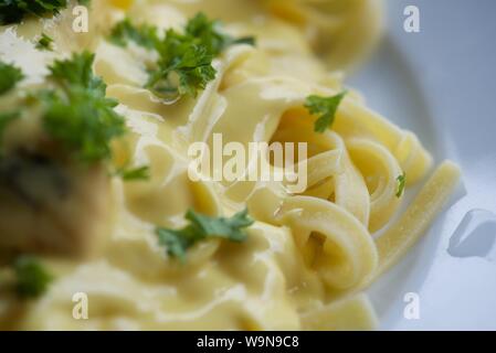 Das Essen : In der Pfanne gebratener Lachs auf einem Bett von Tagliatelle mit Sauce Hollandaise und gehackte Petersilie auf einem weißen Teller serviert Stockfoto