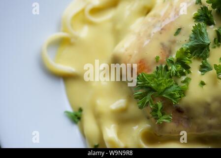 Das Essen : In der Pfanne gebratener Lachs auf einem Bett von Tagliatelle mit Sauce Hollandaise und gehackte Petersilie auf einem weißen Teller serviert Stockfoto