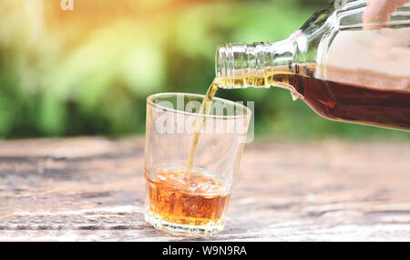 Gießt Whiskey oder Alkohol trinken aus der Flasche und Gläser auf Holz- Hintergrund/Likör Gießen Stockfoto