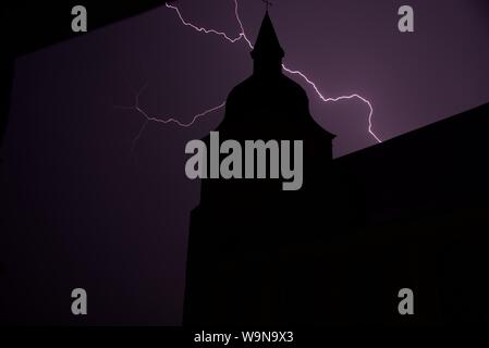 Blitz: Gespaltener Blitz erhellt den Himmel hinter einer ländlichen Kirche im Norden Frankreichs nach einem Tag, wenn Temperaturen erreicht 41˚ Celsius Stockfoto