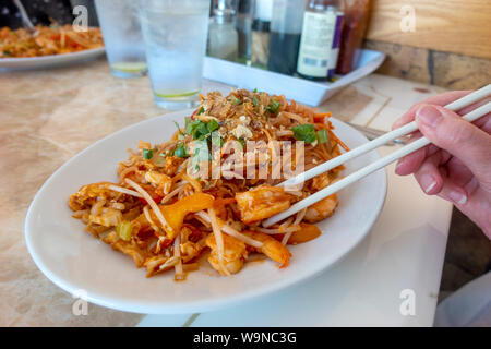 Womans Hände mit Stäbchen und Garnelen und Meeresfrüchte Pad Thai Mahlzeit mit frischem Koriander Stockfoto