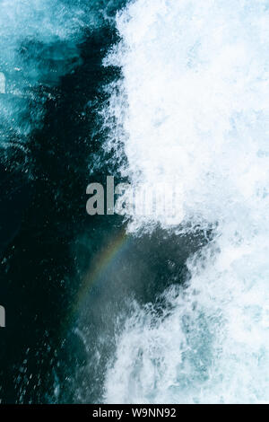 Der kleine Regenbogen erscheint hinter dem Boot in Dunkelblau tobenden Wasser Stockfoto