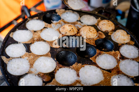 Mörtel - geröstete Gebäck oder "Kanom Krok' ist für traditionelle thailändische Dessert. Frau Hand entfernen Kanom Krok von Herd durch die Löffel. Street Food in Thailand. Thai Stockfoto