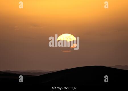 Silhouette von Sanddünen mit der Sonne hinter einer Wolke Stockfoto