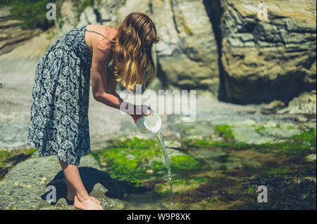 Eine junge Frau wird die Entleerung ein Eimer Wasser am Strand Stockfoto