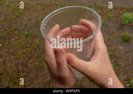 Glas mit Wassertröpfchen in Kid Hände. Junge sammelt Regen fällt. Konzept der Reinen und frischen Wasser, aktiven Lebensstil und Parenting. Ökologie und Stockfoto
