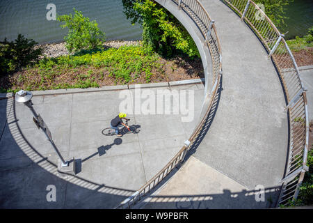 Radfahrer, reitet auf einem Pfad entlang eines Flusses unter einem Oval Brücke. Die Nutzung des Fahrrades als Verkehrsmittel für viele Fans hat sich von einem Hobby gewachsen Stockfoto