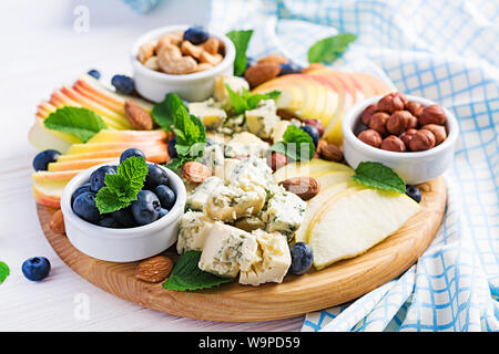 Käseplatte mit verschiedenen Käsesorten, Blaubeere, Äpfel, Nüsse auf weißer Tisch. Italienische Käseplatte und Obst. Stockfoto