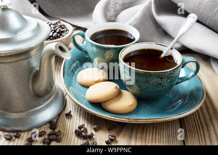 Zwei blaue vintage Tassen schwarzen Kaffee, Keksen und antike Zinn Kaffeekanne von Leinen und Kaffeebohnen auf einem alten Holztisch umgeben Stockfoto