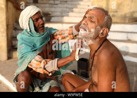 Friseur rasiert eine hinduistische Pilger auf dem ghats in Varanasi, Indien. Varanasi ist das Heiligste der sieben heiligen Städte in Indien Stockfoto