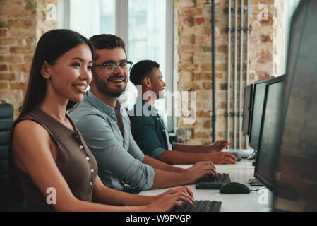 Glücklich zusammen zu arbeiten. Gruppe von fröhlicher junger Mitarbeiter arbeiten an Computern und lächelnd während der Sitzung in moderner, offener Raum. Job Konzept. Geschäftsleute. Arbeitsplatz Stockfoto