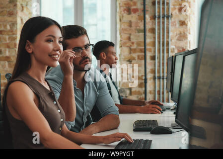 Diskussionen über neue Projekt. Gruppe von fröhlicher junger Mitarbeiter arbeiten an Computern und lächelnd während der Sitzung in moderner, offener Raum. Job Konzept. Geschäftsleute. Arbeitsplatz Stockfoto