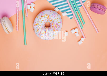 Crwative Komposition mit süßen Leckereien und Party Einrichtung. Donuts, Macarons, Marshmallows und Papier Trinkhalme auf pastellfarbenen Hintergrund Stockfoto